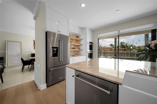 kitchen with light wood-type flooring, stainless steel appliances, white cabinetry, and light stone countertops