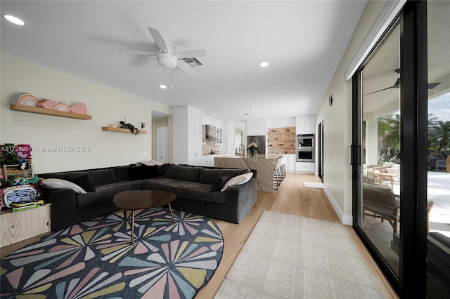 living room featuring light wood-type flooring, ceiling fan, and built in shelves