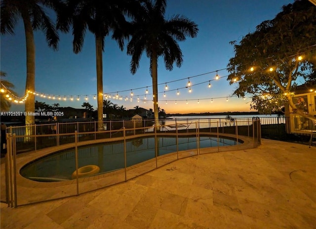 pool at dusk featuring a water view and a patio