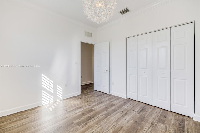 unfurnished bedroom featuring crown molding, an inviting chandelier, a closet, and light hardwood / wood-style floors