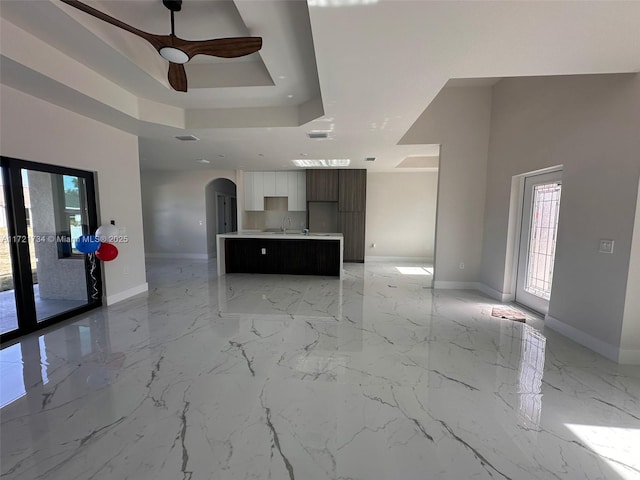 unfurnished living room with arched walkways, baseboards, a ceiling fan, a raised ceiling, and a sink