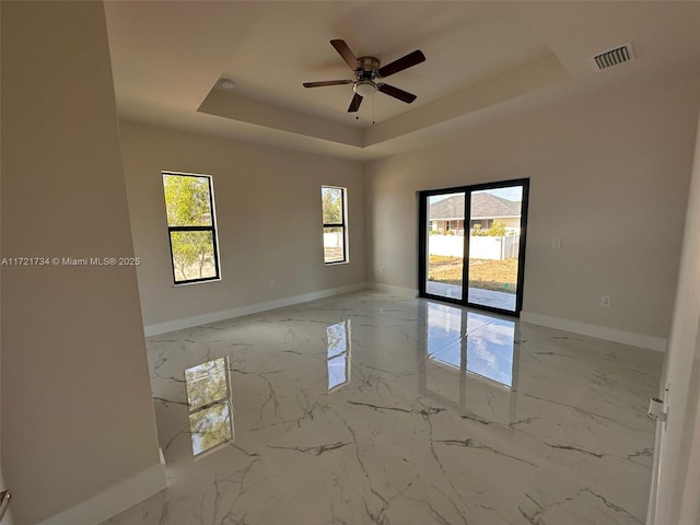 spare room featuring a tray ceiling, baseboards, light marble finish flooring, and ceiling fan