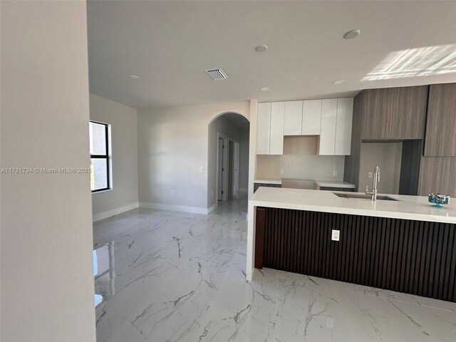 kitchen featuring modern cabinets, a sink, light marble finish flooring, arched walkways, and white cabinetry
