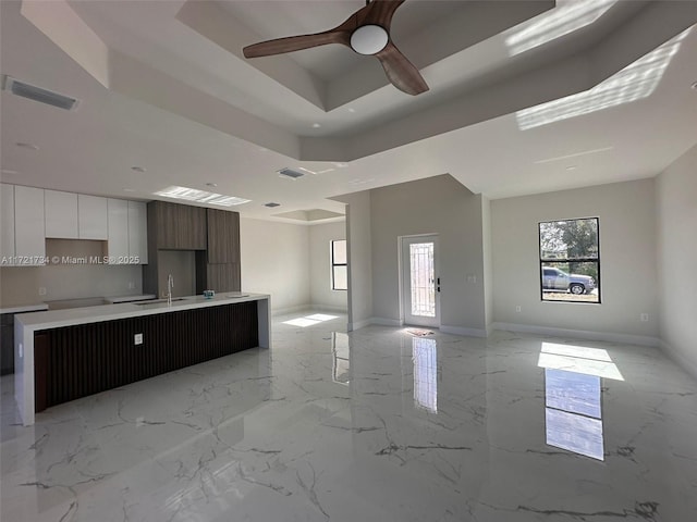 kitchen with a raised ceiling, plenty of natural light, an island with sink, and white cabinets