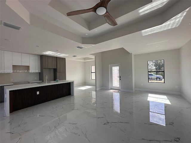 kitchen with modern cabinets, a tray ceiling, open floor plan, light countertops, and ceiling fan