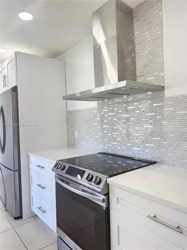 kitchen with appliances with stainless steel finishes, white cabinetry, light stone counters, tasteful backsplash, and wall chimney exhaust hood