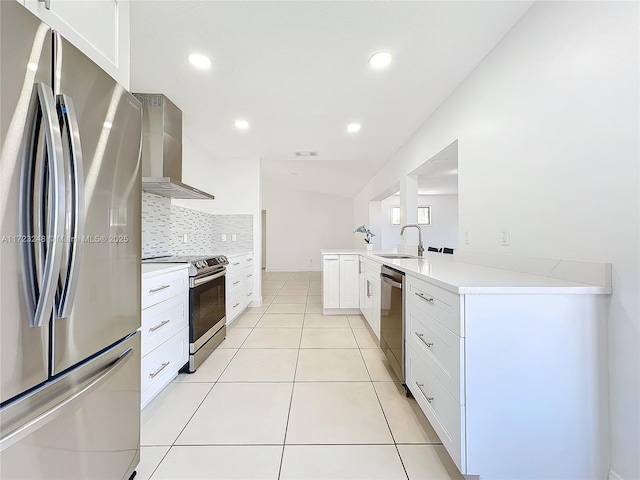 kitchen featuring appliances with stainless steel finishes, tasteful backsplash, white cabinets, kitchen peninsula, and wall chimney exhaust hood