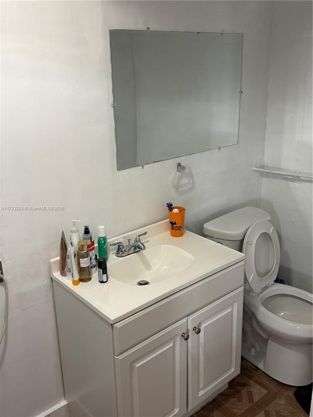 bathroom with parquet flooring, vanity, and toilet