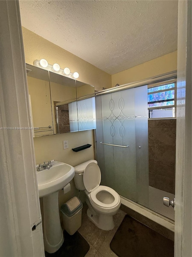 bathroom with tile patterned flooring, a textured ceiling, toilet, and a shower with shower door