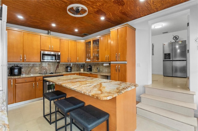 kitchen with decorative backsplash, appliances with stainless steel finishes, light stone countertops, wooden ceiling, and a kitchen island