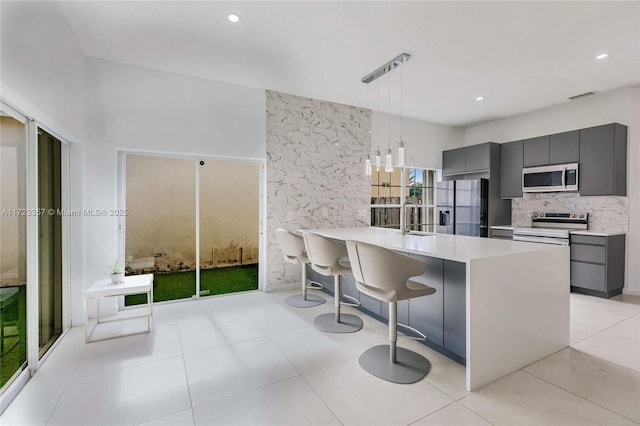 kitchen featuring gray cabinetry, a breakfast bar, pendant lighting, and appliances with stainless steel finishes