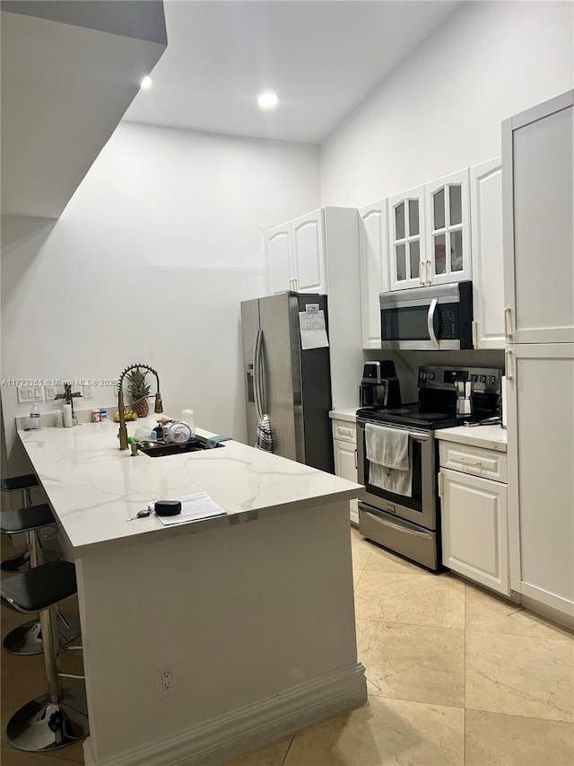 kitchen with white cabinets, a kitchen breakfast bar, light stone countertops, and stainless steel appliances