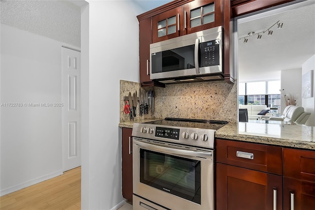 kitchen featuring backsplash, light stone countertops, a textured ceiling, appliances with stainless steel finishes, and light hardwood / wood-style floors