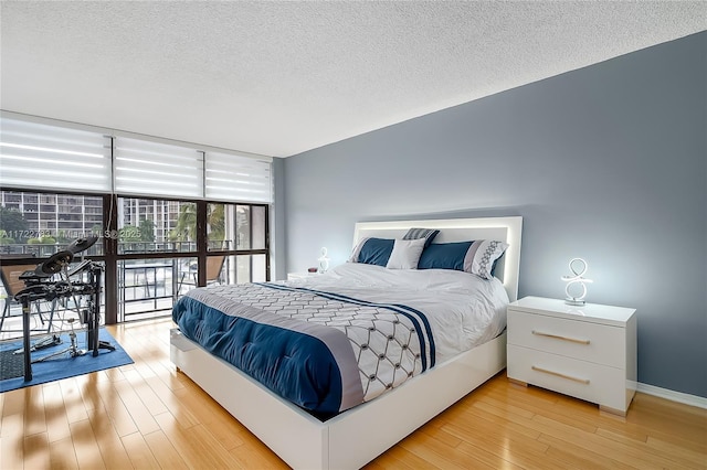 bedroom featuring a wall of windows, light wood-type flooring, and a textured ceiling