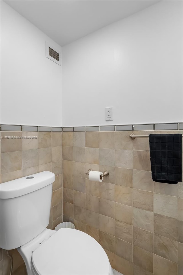 bathroom with toilet and tile walls