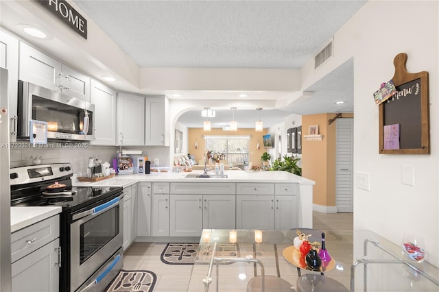 kitchen featuring sink, stainless steel appliances, tasteful backsplash, kitchen peninsula, and a textured ceiling