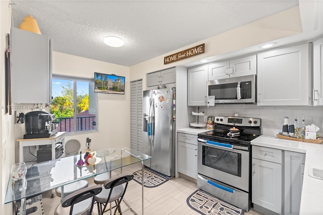 kitchen with backsplash, gray cabinetry, a textured ceiling, stainless steel appliances, and light tile patterned flooring