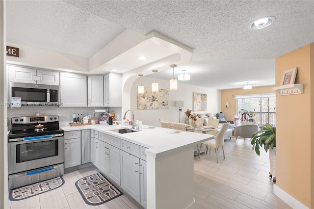 kitchen featuring sink, decorative backsplash, decorative light fixtures, kitchen peninsula, and stainless steel appliances