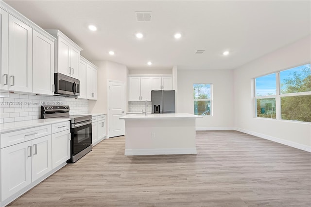 kitchen with a kitchen island with sink, white cabinets, stainless steel appliances, and light hardwood / wood-style floors