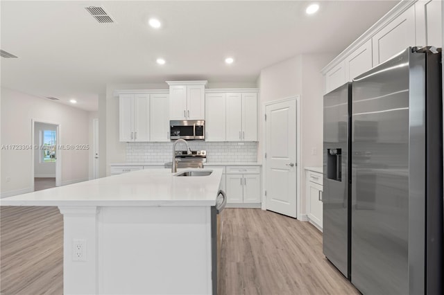 kitchen featuring sink, an island with sink, appliances with stainless steel finishes, light hardwood / wood-style floors, and white cabinetry