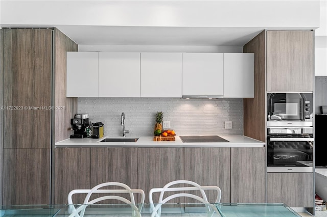 kitchen with backsplash, sink, white cabinets, and black appliances