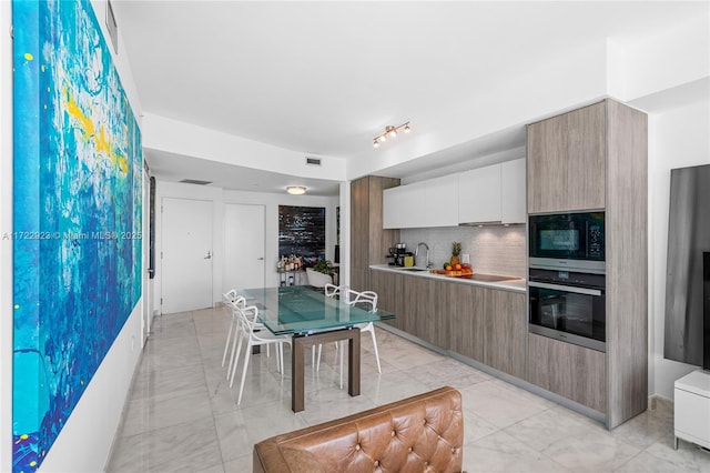 kitchen featuring tasteful backsplash, stainless steel oven, built in microwave, sink, and white cabinetry