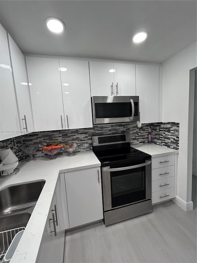 kitchen featuring decorative backsplash, appliances with stainless steel finishes, light stone countertops, sink, and white cabinetry