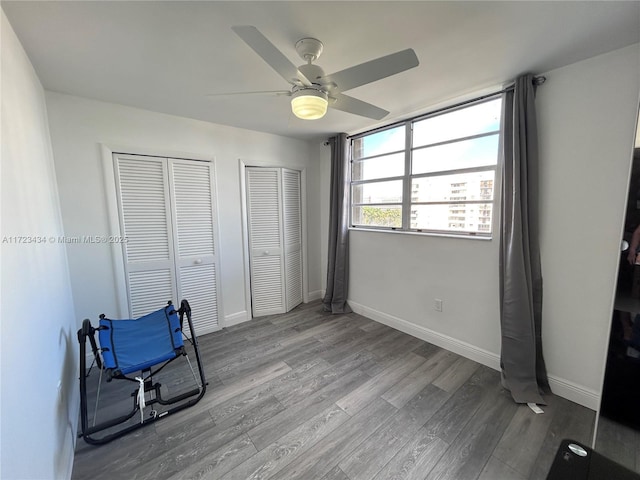 unfurnished bedroom featuring ceiling fan, two closets, and hardwood / wood-style flooring