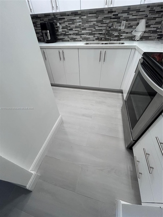 kitchen featuring backsplash, white cabinetry, sink, and stove