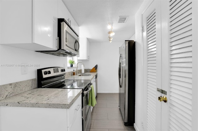 kitchen featuring white cabinets, stainless steel appliances, light stone counters, and sink