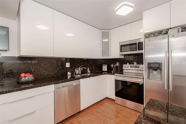 kitchen with light hardwood / wood-style floors, dark stone counters, white cabinets, sink, and stainless steel appliances