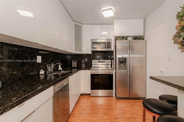 kitchen featuring hardwood / wood-style floors, dishwasher, a kitchen breakfast bar, dark stone countertops, and white cabinetry