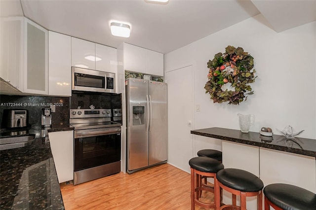 kitchen featuring light hardwood / wood-style floors, appliances with stainless steel finishes, a kitchen breakfast bar, white cabinets, and backsplash