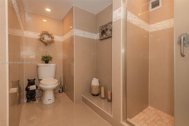 bathroom featuring tiled shower, toilet, tile patterned flooring, and tile walls