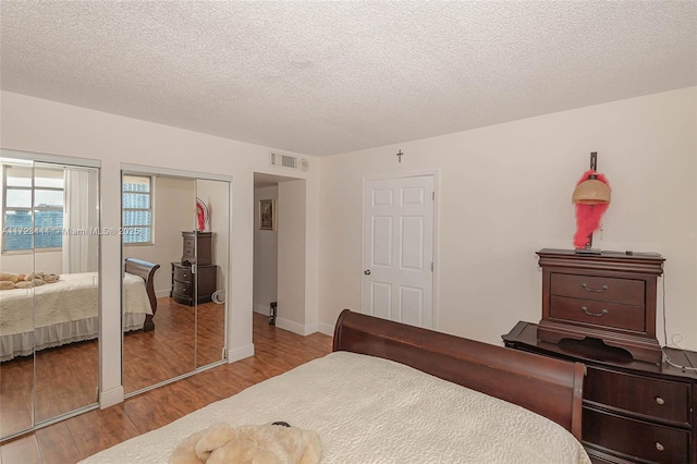 bedroom with light hardwood / wood-style floors, a textured ceiling, and two closets