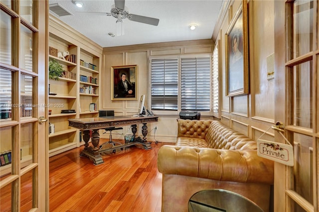 home office with light wood-type flooring, a textured ceiling, built in features, and ceiling fan