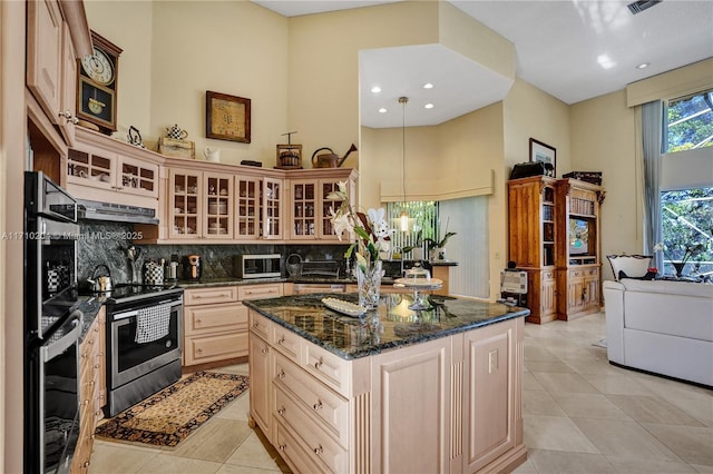 kitchen with stainless steel electric range, dark stone countertops, a towering ceiling, and decorative light fixtures