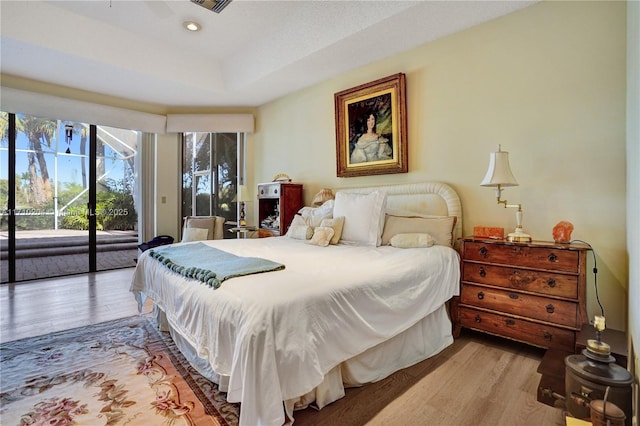 bedroom featuring a raised ceiling, access to exterior, and light hardwood / wood-style floors