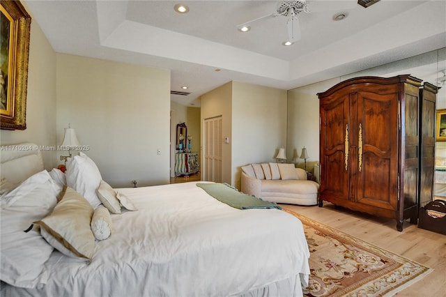 bedroom featuring a tray ceiling, ceiling fan, a closet, and light hardwood / wood-style floors