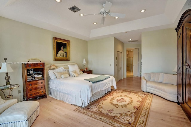 bedroom with ceiling fan, light hardwood / wood-style flooring, and a tray ceiling