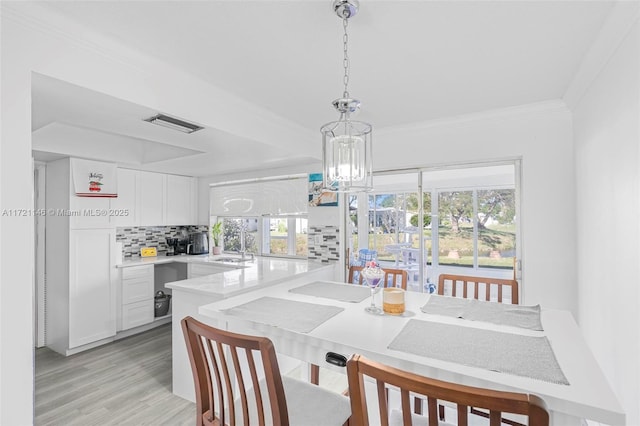 dining space with a chandelier, a healthy amount of sunlight, ornamental molding, and light hardwood / wood-style flooring