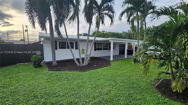 back house at dusk featuring a lawn and a patio area