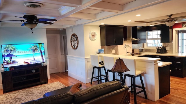 kitchen featuring kitchen peninsula, a breakfast bar, wall chimney exhaust hood, and coffered ceiling