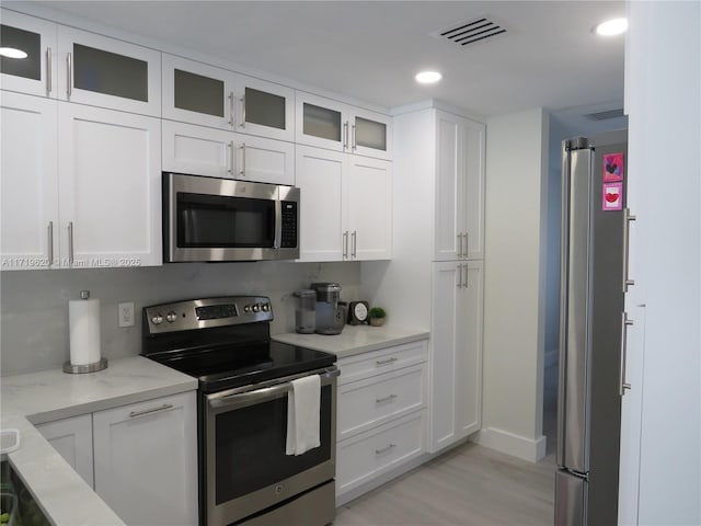 kitchen with light stone countertops, appliances with stainless steel finishes, light wood-type flooring, and white cabinetry