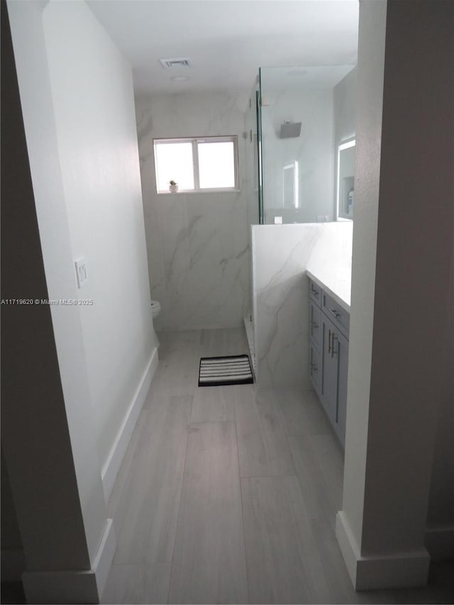 bathroom featuring vanity, toilet, and a tile shower