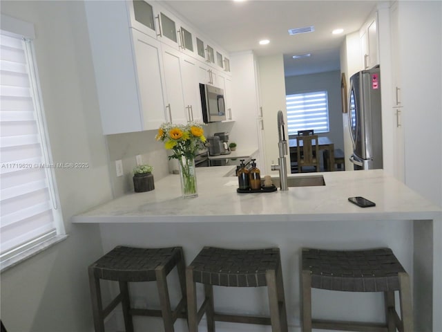 kitchen featuring white cabinetry, sink, kitchen peninsula, a breakfast bar area, and appliances with stainless steel finishes