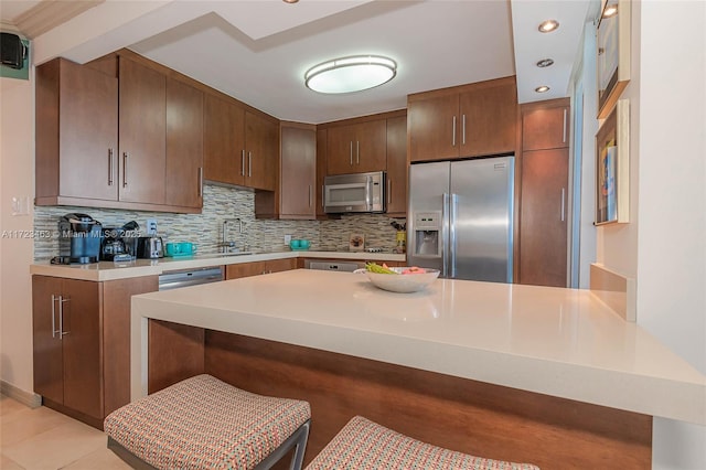 kitchen with tasteful backsplash, kitchen peninsula, a kitchen bar, stainless steel appliances, and light tile patterned floors