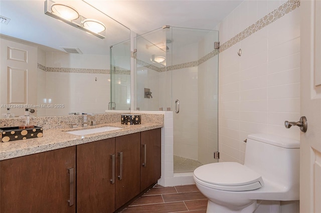 bathroom featuring toilet, tile walls, a shower with shower door, and vanity