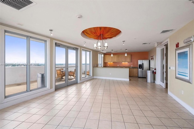 unfurnished living room featuring a water view, light tile patterned floors, a wealth of natural light, and a chandelier