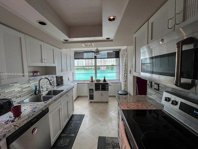 kitchen with sink, a tray ceiling, tasteful backsplash, white cabinetry, and stainless steel appliances